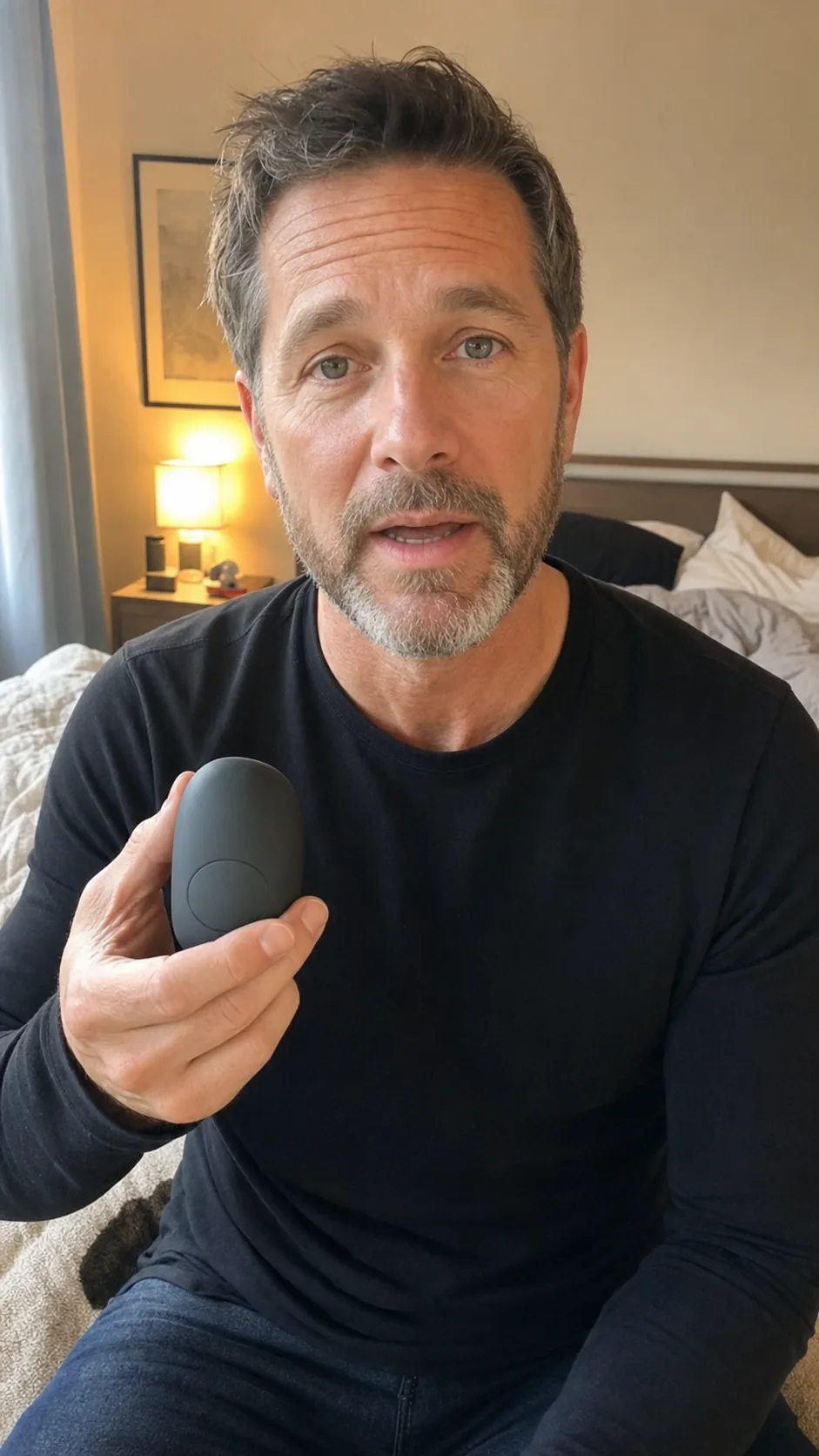 Man in a bedroom records a direct-to-camera clip while holding a discreet unbranded wellness device.
